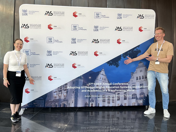 Olga Wagner (links) und Uwe Wilkesmann (rechts) stehen vor dem Poster der CHER Konferenz.